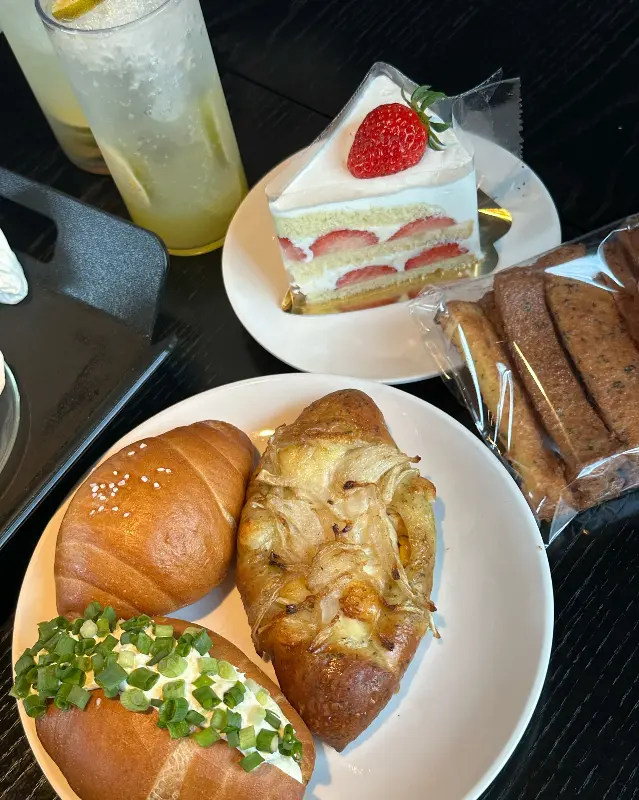 테이블 위에 놓인 빵과 음료. 창녕 양파빵과 딸기 케이크, 에이드가 보인다.