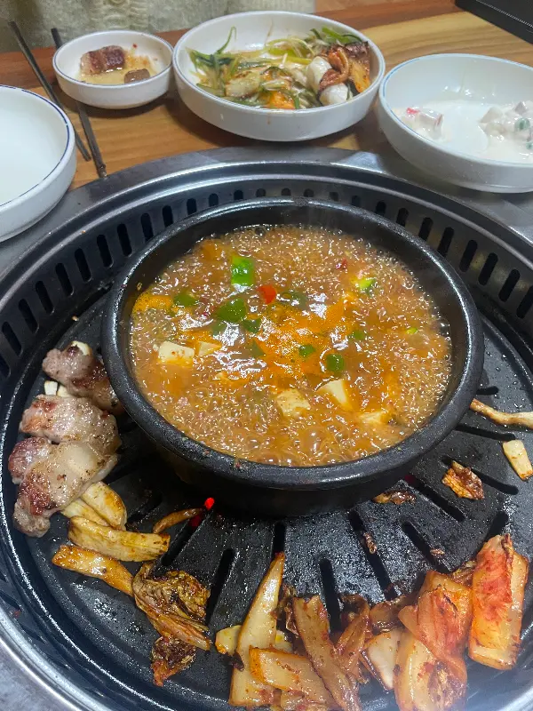 불판 위에서 삼겹살, 김치, 된장찌개가 함께 끓고 있는 모습
