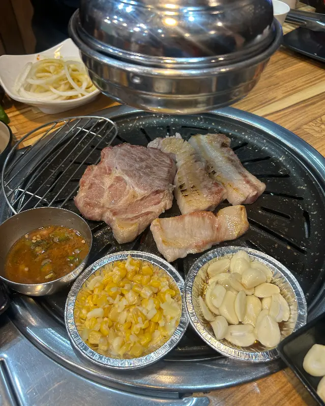 불판 위에 삼겹살과 마늘, 콘치즈가 함께 구워지는 사진