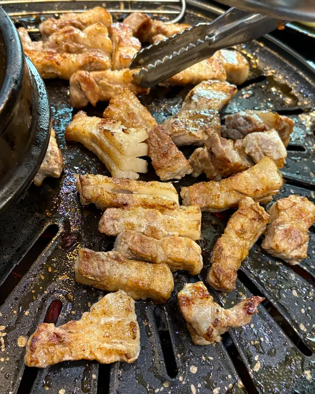 잘 익은 삼겹살을 집게로 자르는 사진