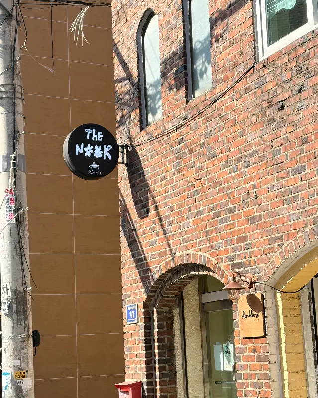 붉은 벽돌 건물 외관에 걸린 카페 더눅 간판