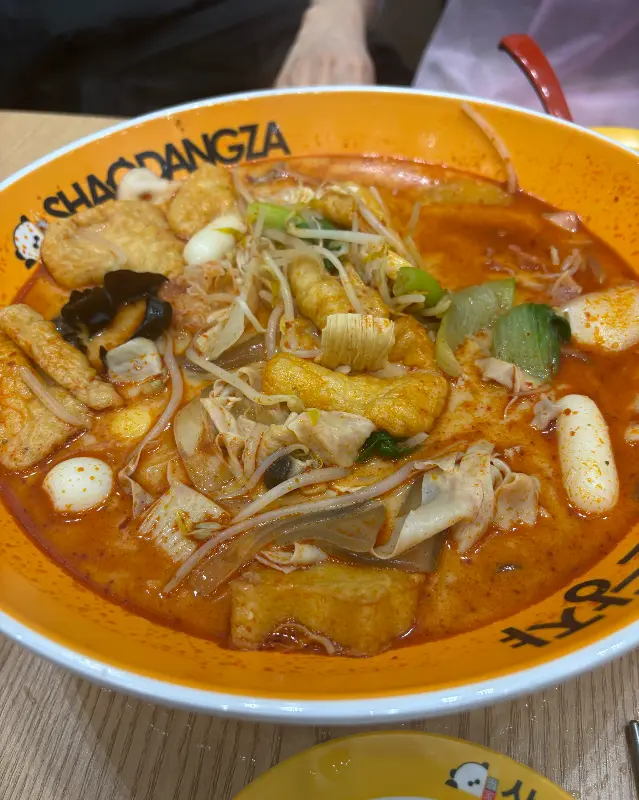 노란색 그릇에 담긴 마라탕. 다양한 종류의 면과 채소, 꼬치가 가득 담겨 있다.