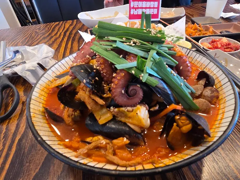 홍합과 바지락이 푸짐하게 들어간 짬뽕 위에 문어 다리가 통째로 올려져 있고, 신선한 부추가 곁들여져 있다.