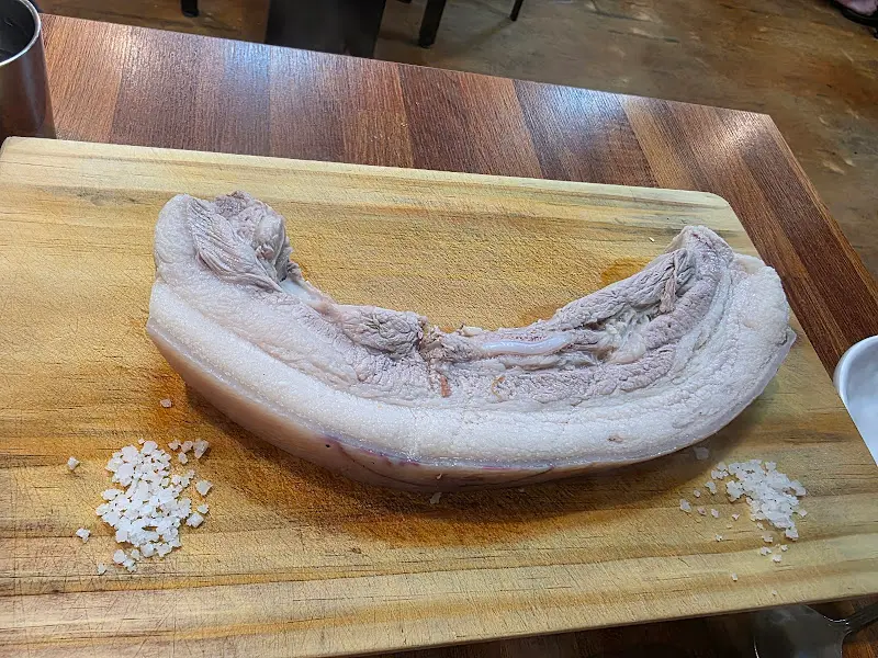 커다란 흑돼지 오겹살 덩어리가 나무 도마 위에 놓인 모습