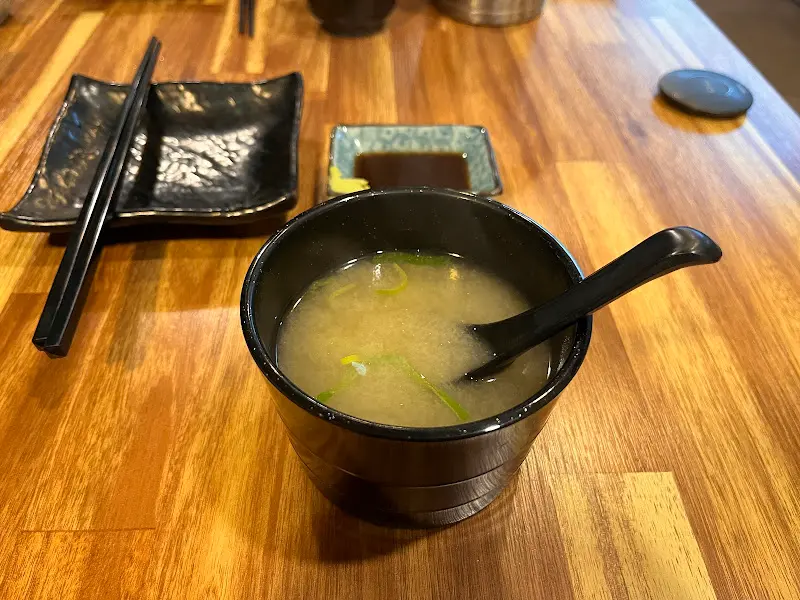 미소 장국이 담긴 검은색 그릇과 젓가락, 간장 종지가 나무 테이블 위에 놓여 있는 모습