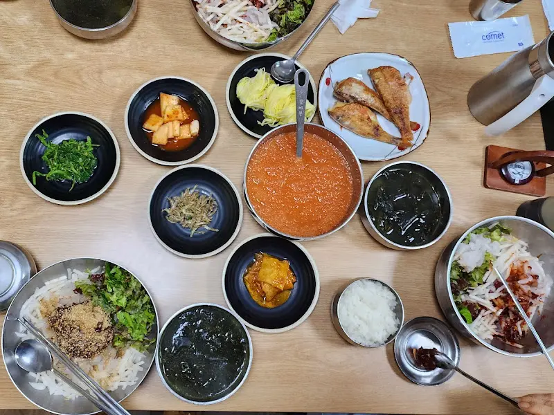 테이블 위에 놓인 다양한 밑반찬과 물회, 밥, 물통 등의 모습