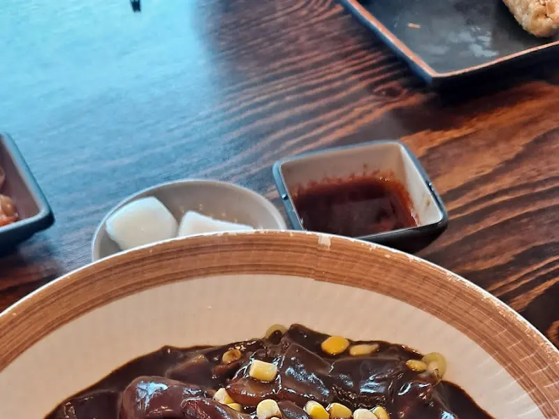 테이블 위 짜장면, 윤기가 흐르는 짜장 소스와 옥수수 알갱이가 뿌려져 있다.