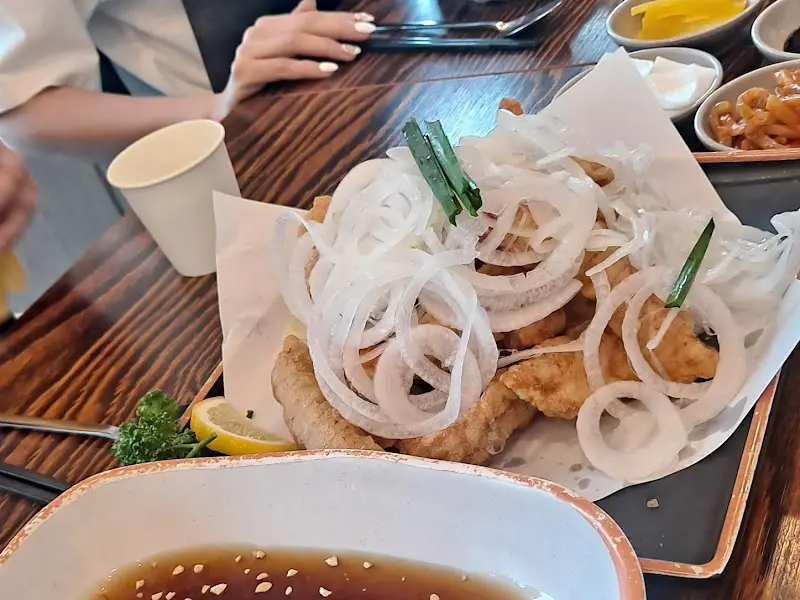 테이블 위에 놓인 탕수육, 얇게 썰린 양파와 함께 제공되며 소스 그릇에는 깨가 뿌려져 있다.