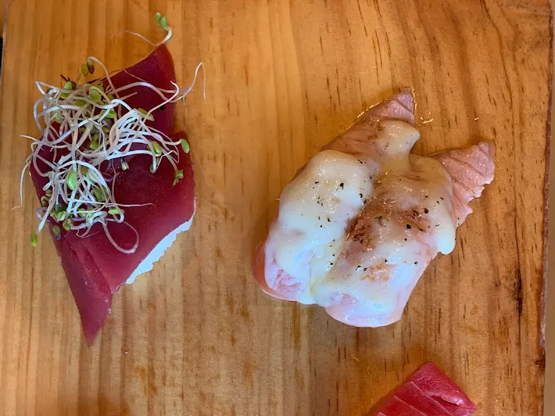 붉은 빛깔이 아름다운 참치 초밥과 흰색 소스가 뿌려진 초밥이 나무 도마 위에 놓여 있는 모습