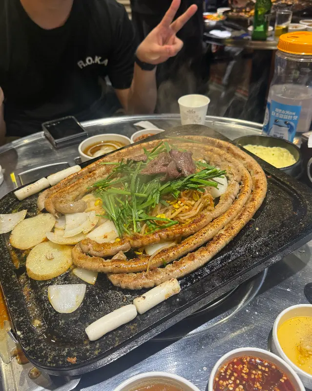 돌판 위에 길게 늘어진 대창과 함께 떡, 양파, 김치 등이 놓여 있는 모습