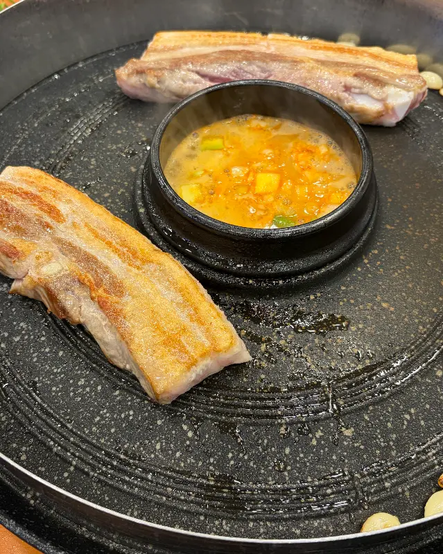 솥뚜껑에 구워지고 있는 삼겹살과 된장찌개