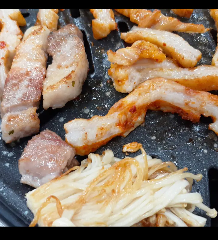 노릇하게 구워진 삼겹살과 팽이버섯의 근접샷