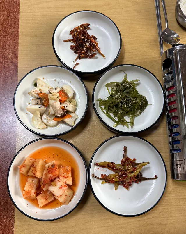 다섯 종류의 반찬이 담긴 접시들이 테이블 위에 놓여 있다. 반찬들은 정갈하게 담겨 있다.