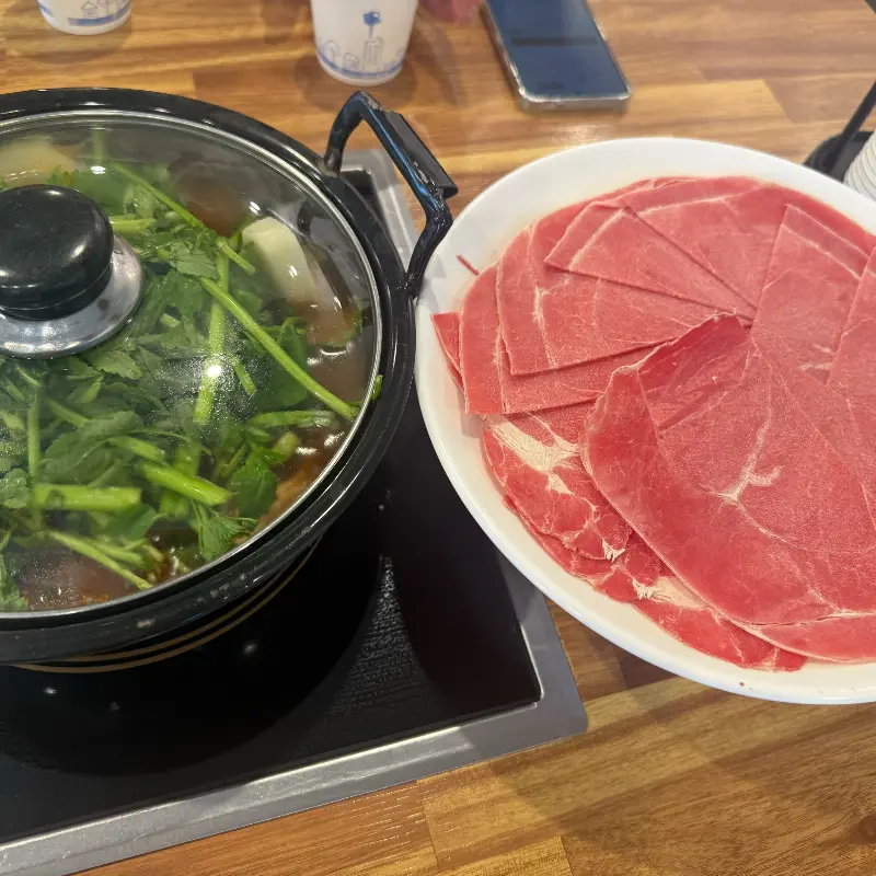 미나리가 듬뿍 올려진 샤브샤브 육수 냄비와 붉은 빛깔의 소고기 접시