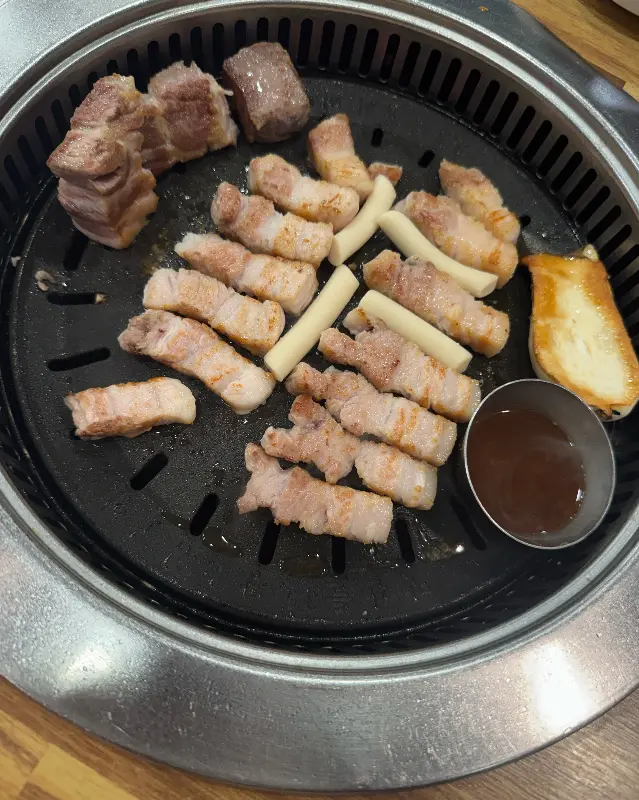 불판 위에서 지글지글 익어가는 삼겹살과 떡의 모습