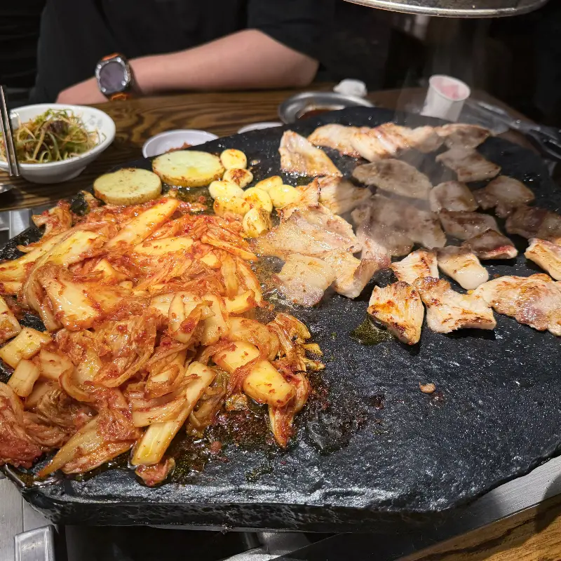 돌판 위에 김치, 마늘, 고기가 구워지는 모습