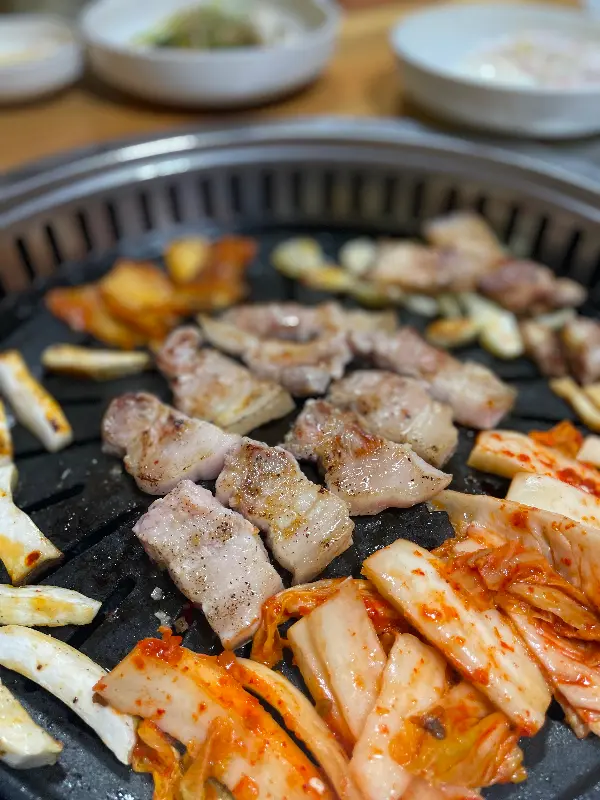 잘 구워진 삼겹살과 김치가 불판 위에 놓여있는 모습