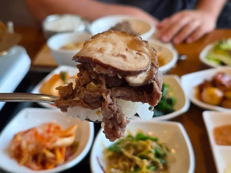 밥 위에 불고기와 버섯을 올려 숟가락으로 뜨고 있는 모습