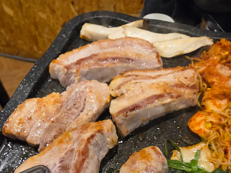 불판 위에서 맛있게 익어가는 삼겹살과 미나리