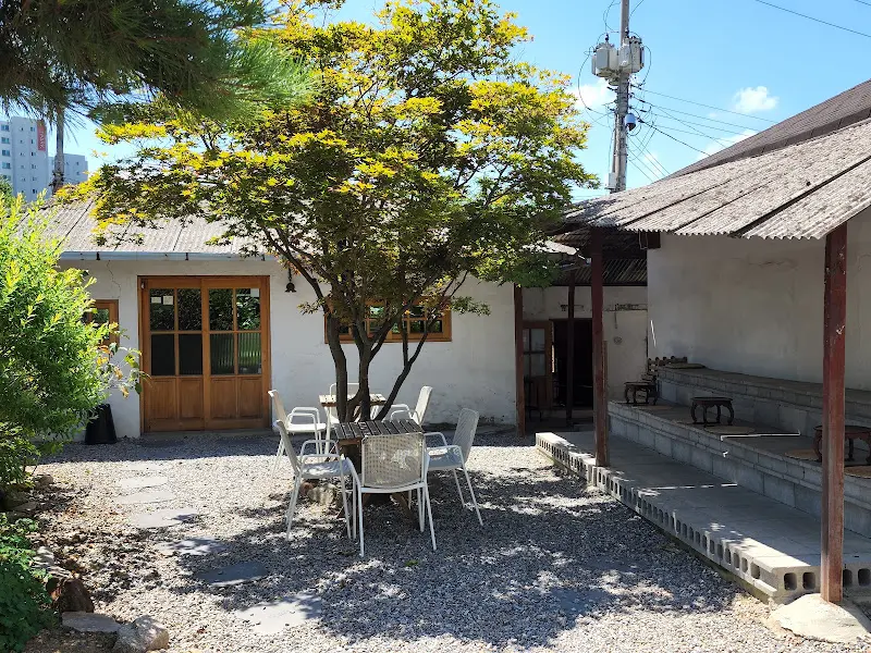 카페 외부 전경. 푸른 나무와 낡은 건물이 조화롭게 어우러져 아름다운 풍경을 만들어낸다.