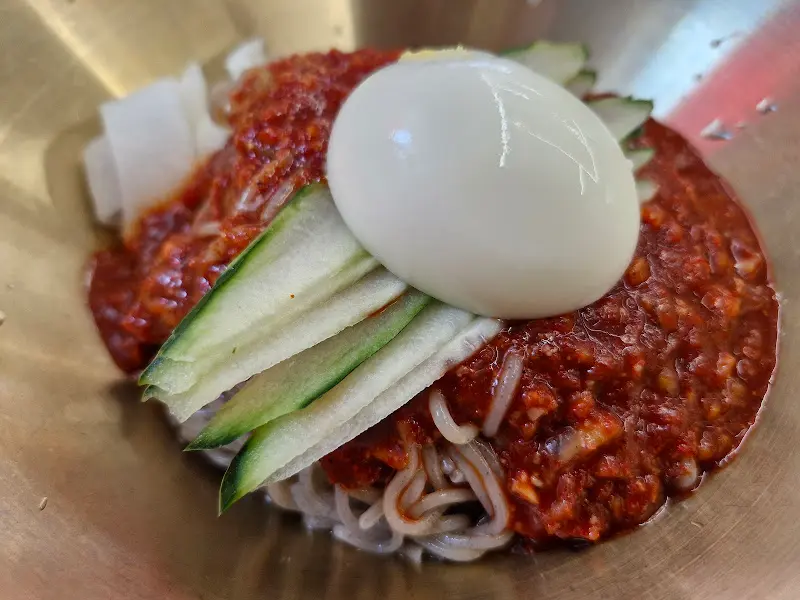 매콤한 양념이 듬뿍 올려진 비빔밀면. 삶은 계란과 오이 고명이 함께 제공된다.