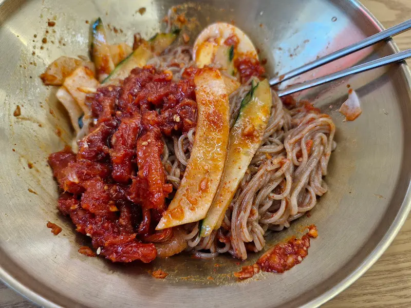 비빔밀면을 젓가락으로 비비는 모습. 붉은 양념이 면에 잘 배어있다.