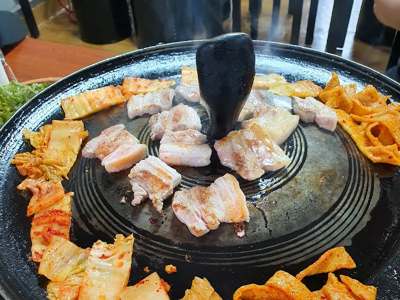 솥뚜껑에 김치와 돼지고기를 함께 구워먹는 모습