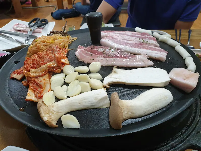 솥뚜껑에 구워지는 삼겹살, 김치, 콩나물, 버섯, 마늘