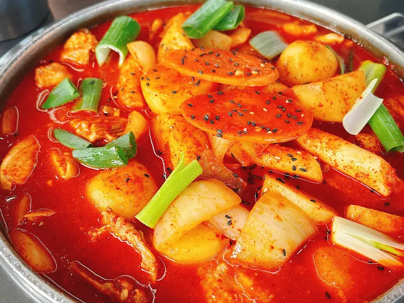 닭볶음탕의 클로즈업 사진. 붉은 국물과 큼지막한 감자, 떡, 파가 보인다.