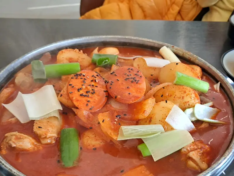 닭볶음탕의 클로즈업 사진. 붉은 국물과 큼지막한 감자, 떡, 파가 보인다.