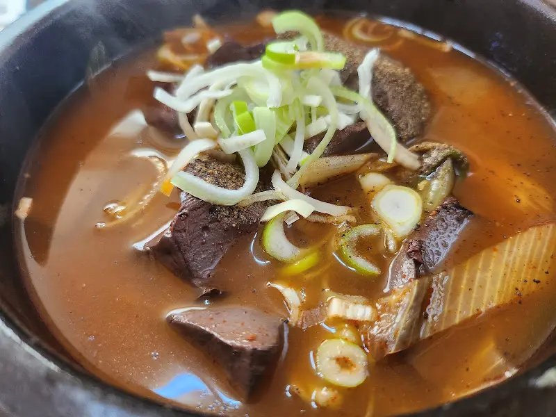 선지해장국이 검은 뚝배기에 담겨 있고, 신선한 파가 고명으로 올려져 있다.