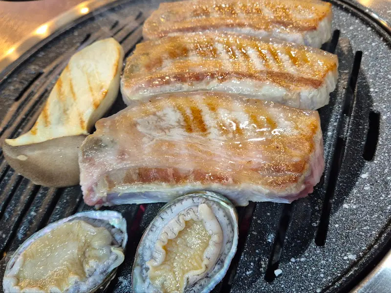 숯불 위에 구워지고 있는 흑돼지 오겹살과 전복