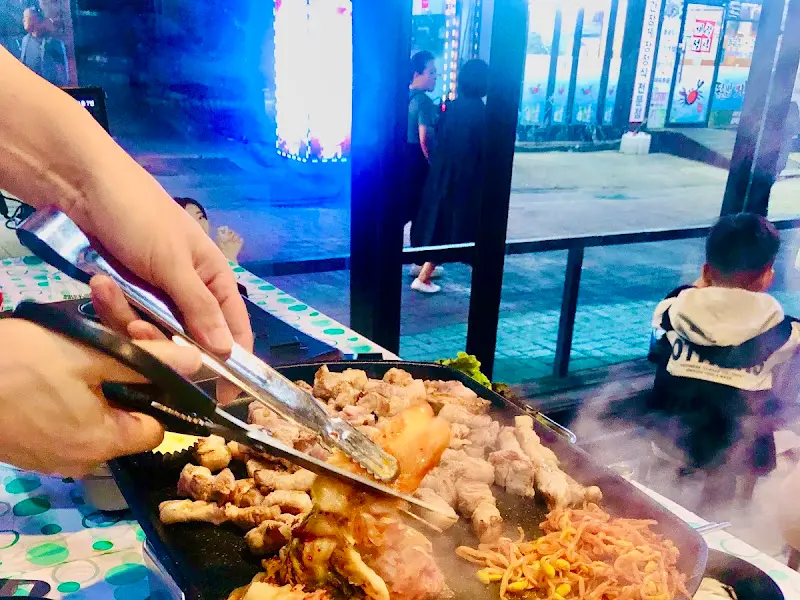 불판 위에서 김치, 콩나물과 함께 구워지는 초벌 삼겹살