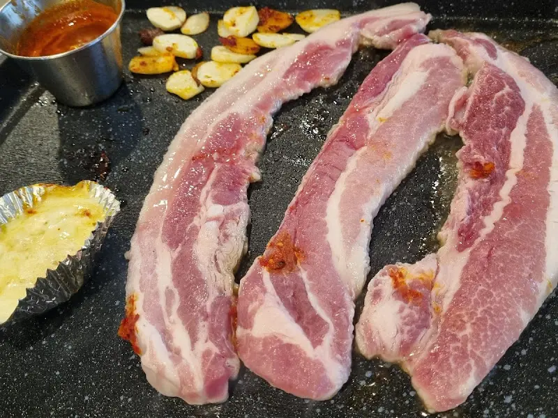 불판 위에 삼겹살, 김치, 마늘이 함께 구워지는 모습