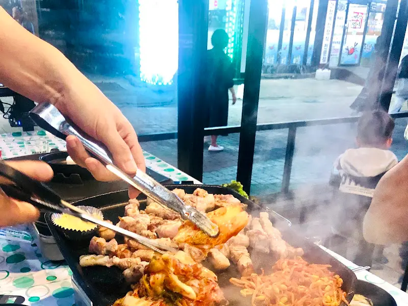 불판 위에서 익어가는 삼겹살을 집게로 들어올리는 모습