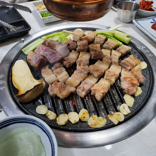 불판 위에 삼겹살과 버섯, 마늘이 함께 구워지고 있다.