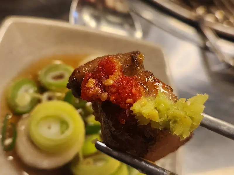 잘 구워진 목살에 와사비와 빨간 양념을 올려 젓가락으로 집은 모습