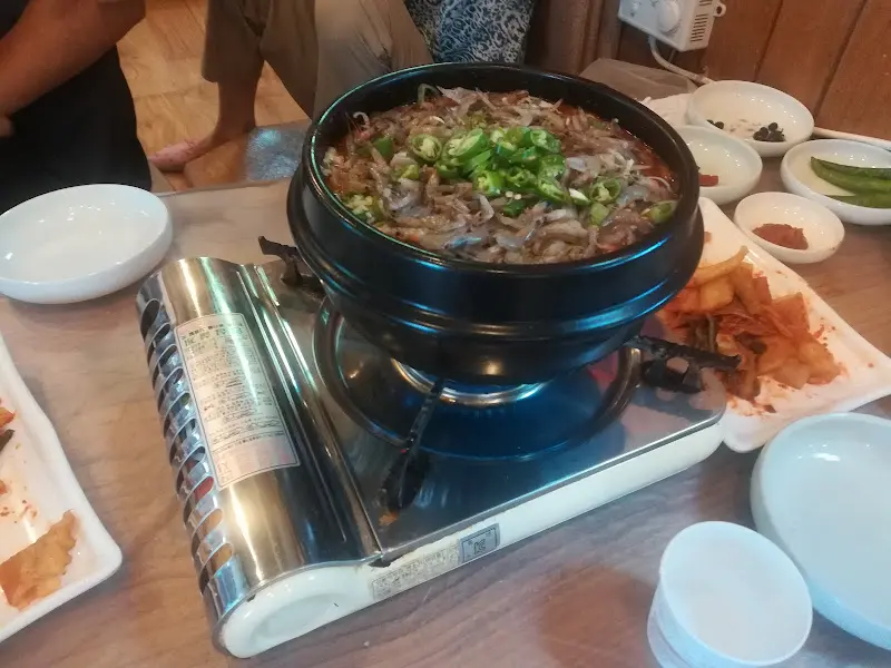 버너 위에 올려진 메기 매운탕 냄비의 모습. 쑥갓이 푸짐하게 올려져 있고, 국물이 끓고 있다.