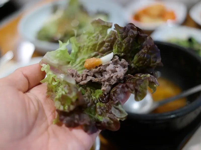 상추에 불고기를 싸서 손으로 들고 있는 모습