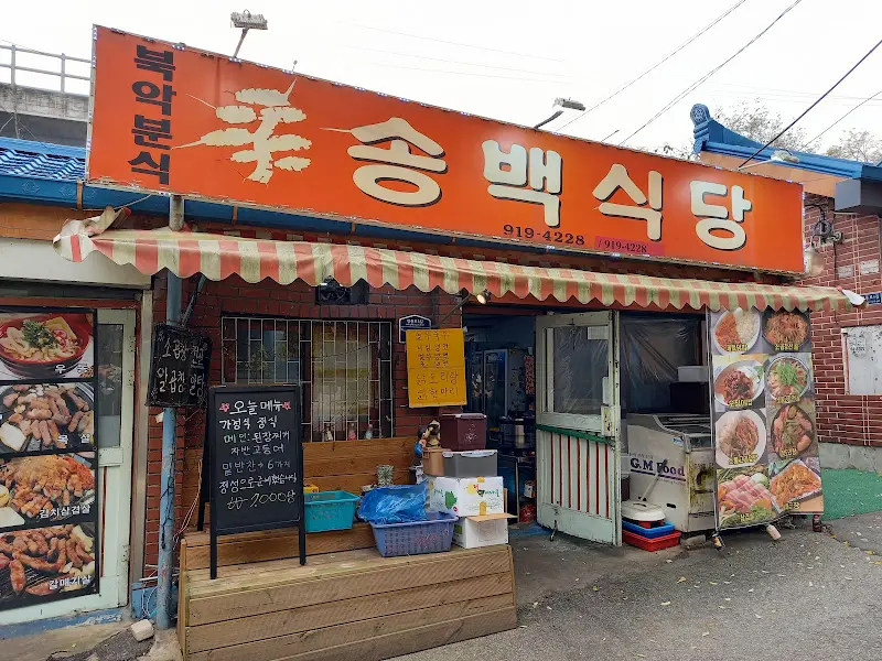 다양한 메뉴 사진이 붙어있는 송백식당 외부 모습