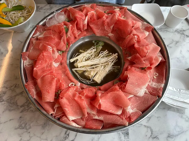 테이블 중앙의 육수를 중심으로 얇게 썰린 소고기가 가득 담긴 접시