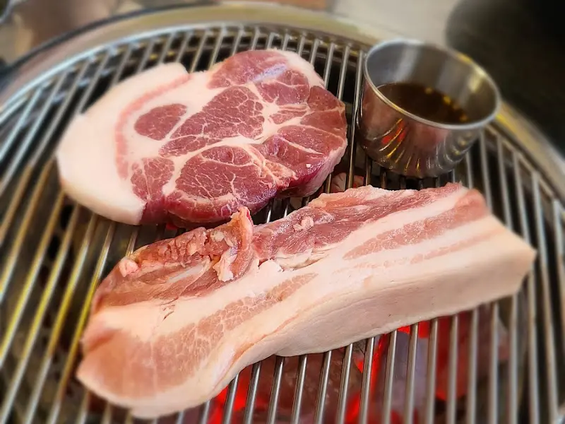 두툼한 흑돼지 목살이 숯불 위에서 노릇하게 익어가는 모습