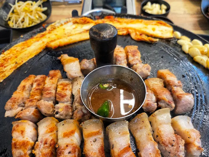 솥뚜껑 가득 구워진 삼겹살과 김치, 마늘