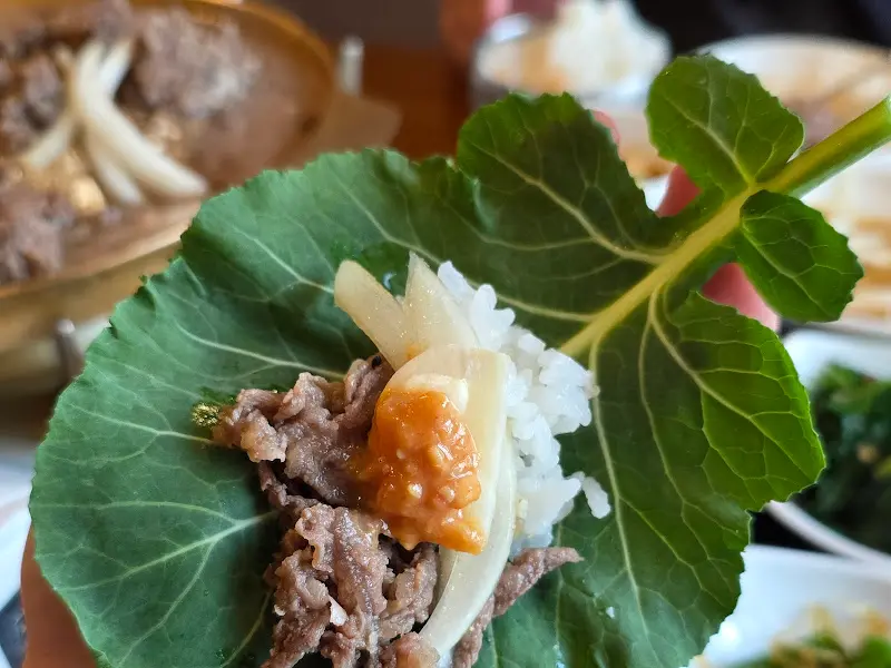 배춧잎에 밥, 불고기, 양파를 올려 싸 먹는 모습
