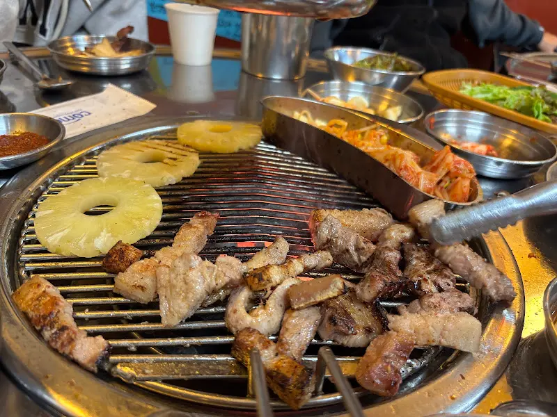 불판 위에서 맛있게 구워지고 있는 돼지고기. 파인애플과 버섯도 함께 구워 먹으면 더욱 풍성한 맛을 즐길 수 있다.