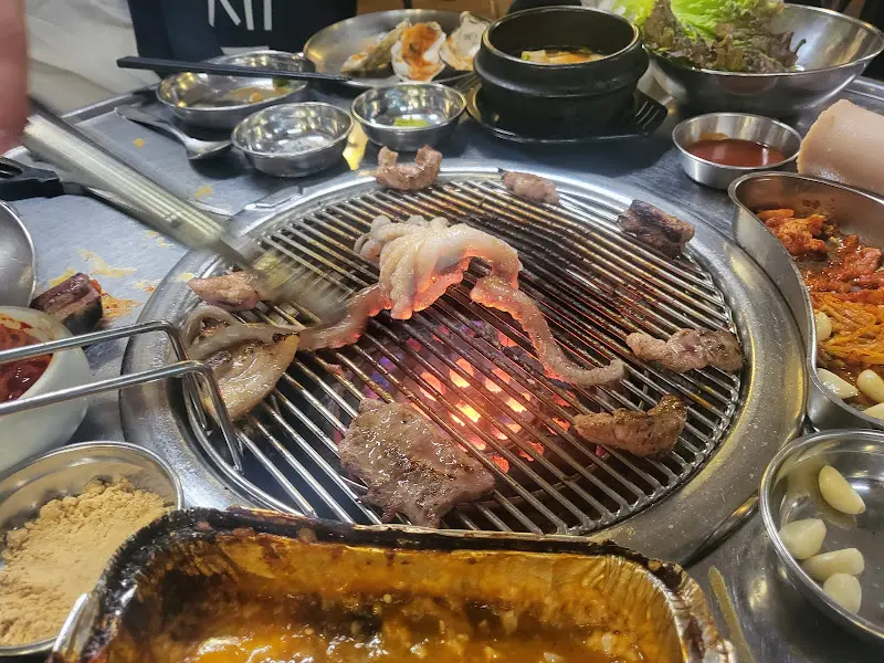 불판 위에서 노릇하게 익어가는 삼겹살과 항정살, 그 옆에 키조개와 낙지가 함께 구워지고 있는 모습