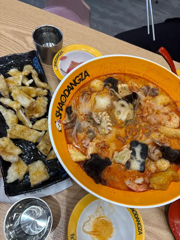 노란색 그릇에 담긴 마라탕과 검은색 접시에 담긴 꿔바로우가 나무 테이블 위에 놓여 있다. 마라탕에는 다양한 재료가 푸짐하게 담겨 있고, 꿔바로우는 먹기 좋게 잘려 있다.