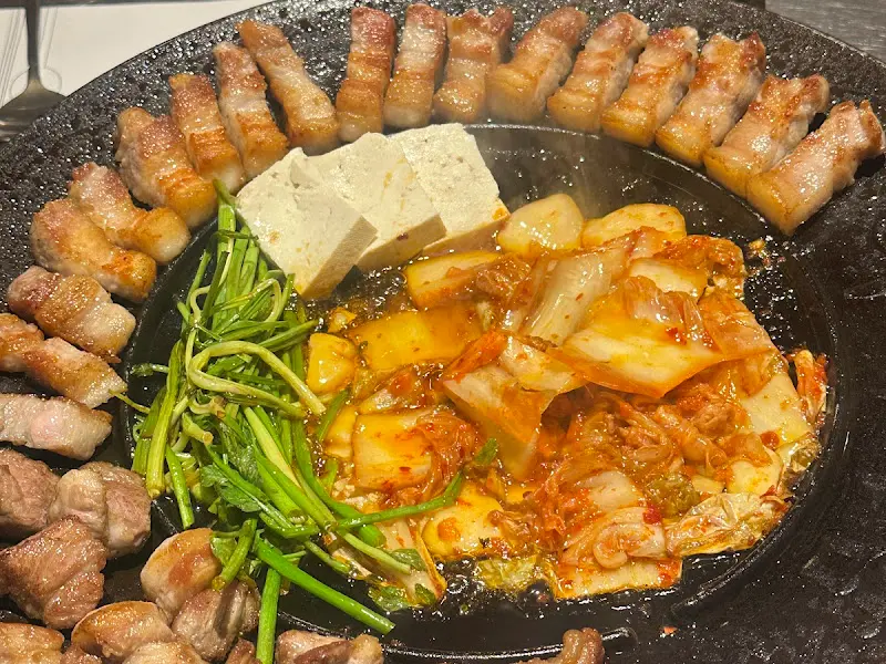 무쇠 솥뚜껑 위 삼겹살, 김치, 미나리, 두부의 조화