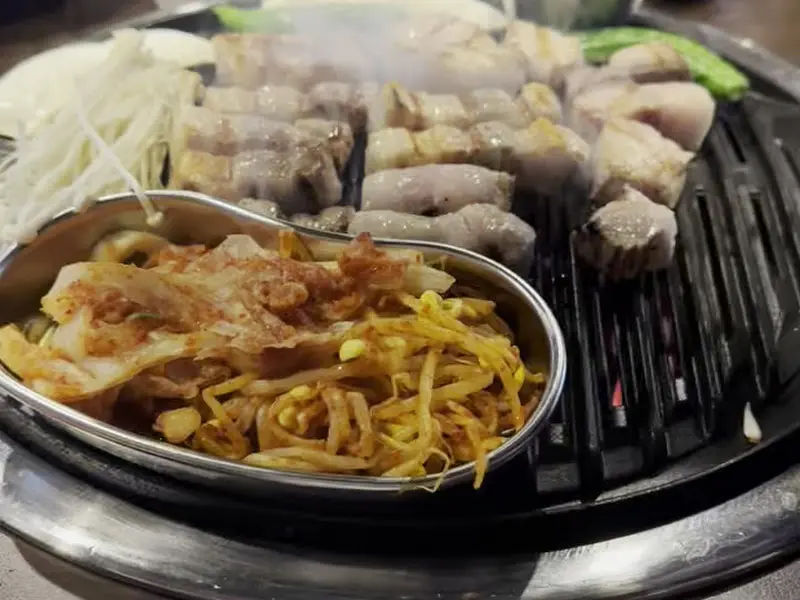 불판에 구워지는 삼겹살과 김치, 콩나물