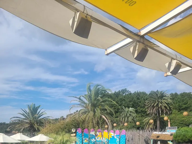 파라솔 아래 테이블과 의자가 놓여 있고, 멀리 푸른 바다가 보이는 사진